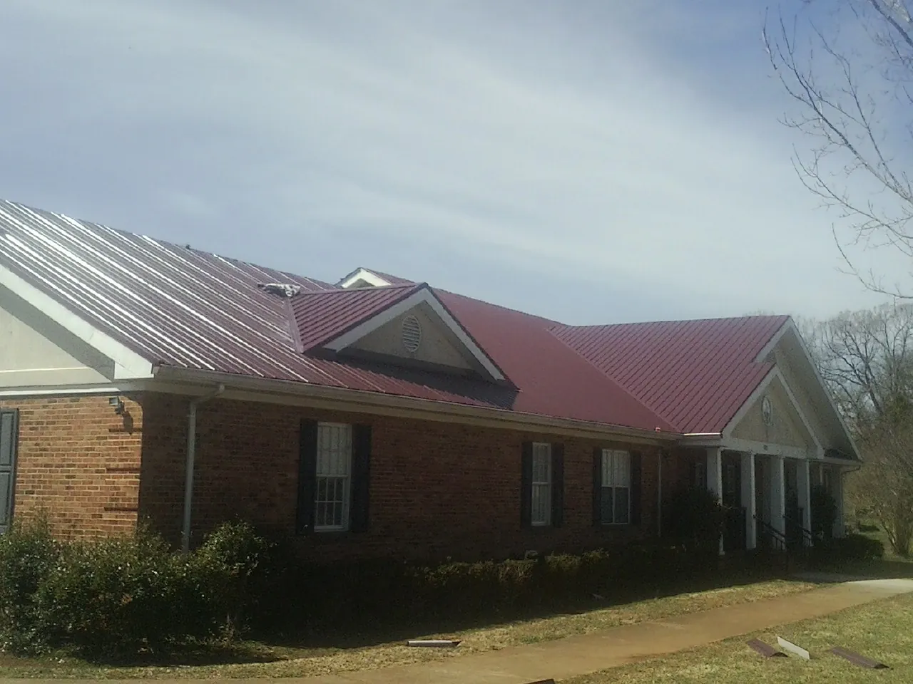 Red metal roof with gabled entries on a long brick building, from a Hail Damage Roof Repair job in Jamul