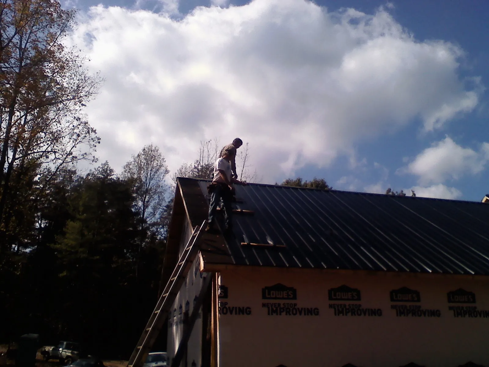 Roofer fastening dark metal panels high against a cloudy sky, from a Roof Inspection job in Jamul